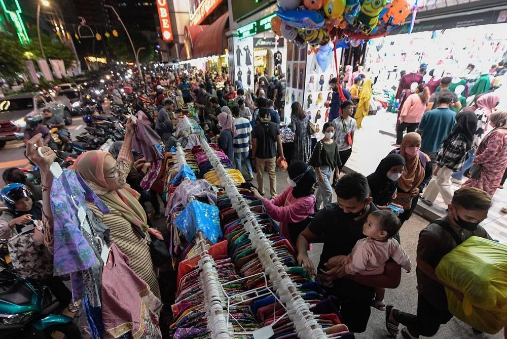 Seorang penjual mempromosikan pakaian kanak-kanak sempena Aidilfitri tidak lama lagi yang dijual dengan harga lelong iaitu RM10 untuk setiap pasang di sekitar Jalan Tuanku Abdul Rahman. - Foto Bernama