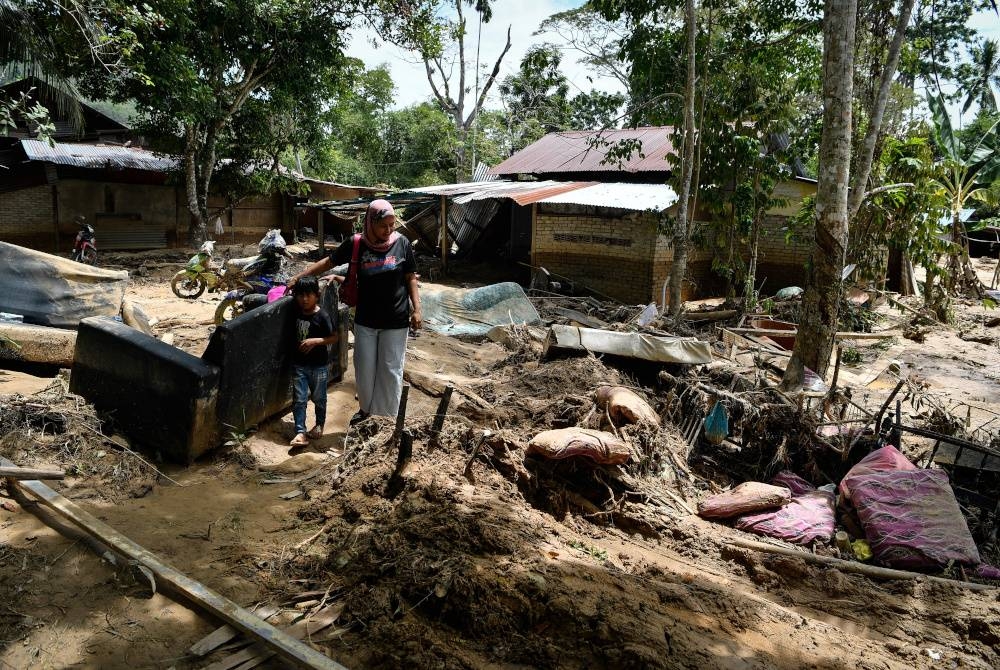 Seorang penduduk Nurul Atikah Ismail, 30, melihat keadaan rumah ibunya di Kampung Iboi, Baling yang rosak serta ditenggelami selut selepas dilanda banjir petang Isnin.