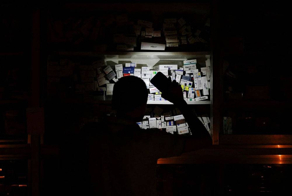 Seorang jurujual kedai farmaseutikal menggunakan cahaya daripada telefon bimbitnya untuk mencari ubat semasa gangguan
bekalan elektrik di Dhaka.