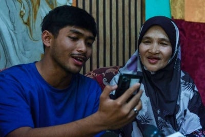 Bekas pelajar Maktab Rendah Sains MARA (MRSM) Jeli, Mohamad Solihin Mohd Nasir, 19, (kiri) ditemani ibunya, Faridah Mohamad, 60, (kanan) menjawab panggilan video daripada Pengerusi Majlis Amanah Rakyat (MARA), Datuk Seri Dr Asyraf Wajdi Dusuki ketika ditemui pemberita di Kampung Kubang Keranji, Pasir Tumboh.