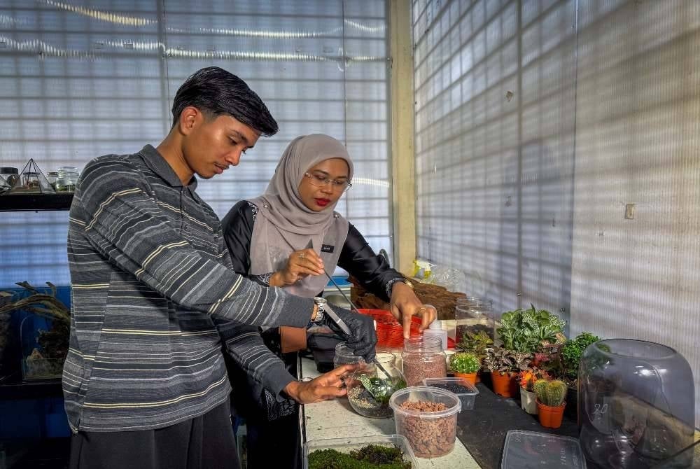 Pensyarah Teknologi Akuakultur selaku Penasihat Kelab Green Vista Zalina Che Manan (kanan) membantu Muhammad Syukur menyusun elemen tumbuhan dan hiasan bagi menghasilkan rekaan terrarium. Foto Bernama