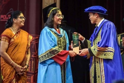 Shamsuri (kanan) menyampaikan Anugerah Ketua Pengarah kepada graduan Diploma Teknologi Digital Politeknik Tuanku Syed Sirajuddin (PTSS), Teerti Ganapathi Rao, 22, sambil disaksikan ibunya, Subuletchumy Muniandi (kiri).