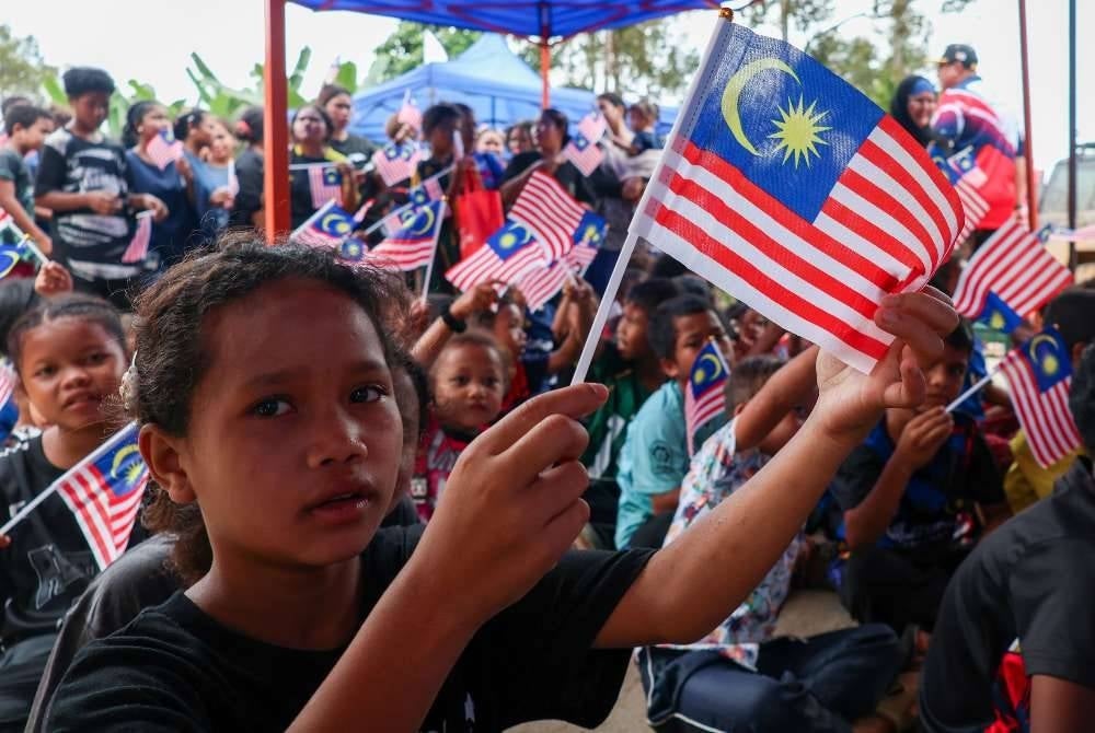 Kanak-kanak masyarakat Orang Asli suku kaum Temiar mengibarkan Jalur Gemilang sambil menyanyikan lagu patriotik sempena Program ‘Be Ades Ma Kampung’ di Kampung Tapai, Pos Hau.