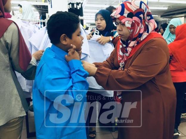 Nor Esah membantu anaknya, Mohd Afizuddin mencuba pakaian sekolah yang baharu di pasaraya Mydin hari ini.
