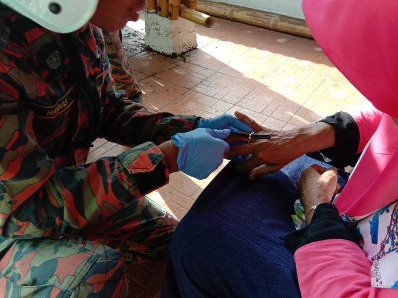 Anggota bomba sedang menanggalkan cincin emas di jari manis warga emas berkenaan. - Foto Ihsan Bomba