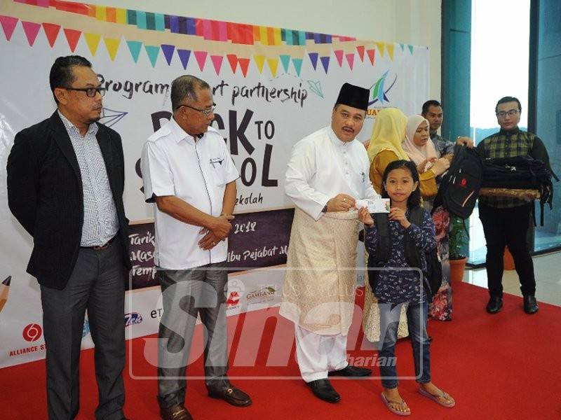 Fadzilla (tiga, kiri) menyampaikan sumbangan peralatan sekolah kepada salah seorang pelajar.