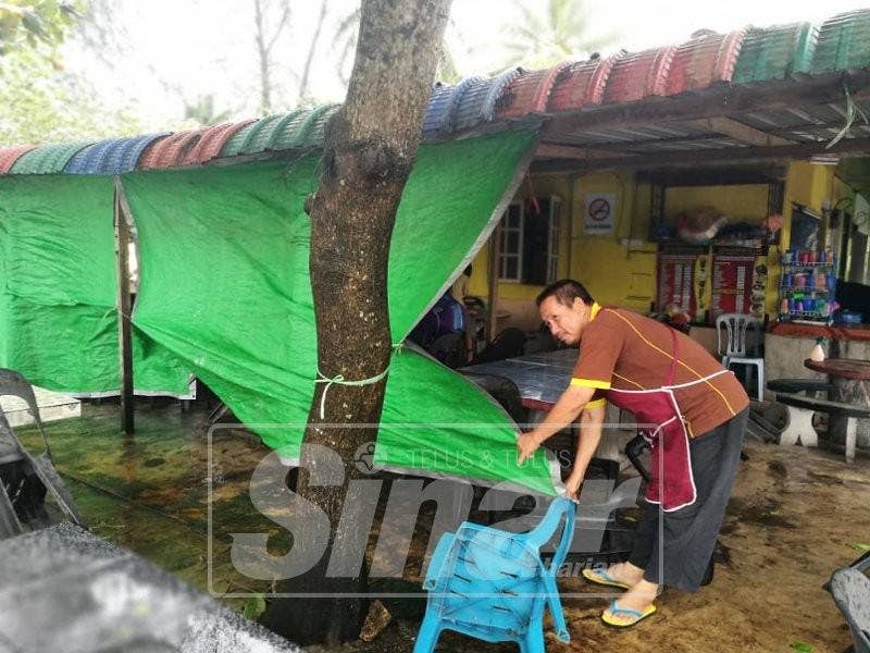 Abdul Rahman memasang tabir menggunakan kanopi untuk mengelakkan angin daripada menerbangkan pinggan mangkuk di gerainya.