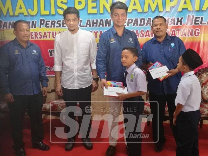 Muhammad Faiz (tengah) menyempurnakan gimik penyerahan sumbangan bantuan persekolahan daripada LKIM kepada 100 pelajar keluarga nelayan Matang sambil diiringi Hasnul Zulkarnain (dua, kiri) dan Raja Kahalid (kiri).