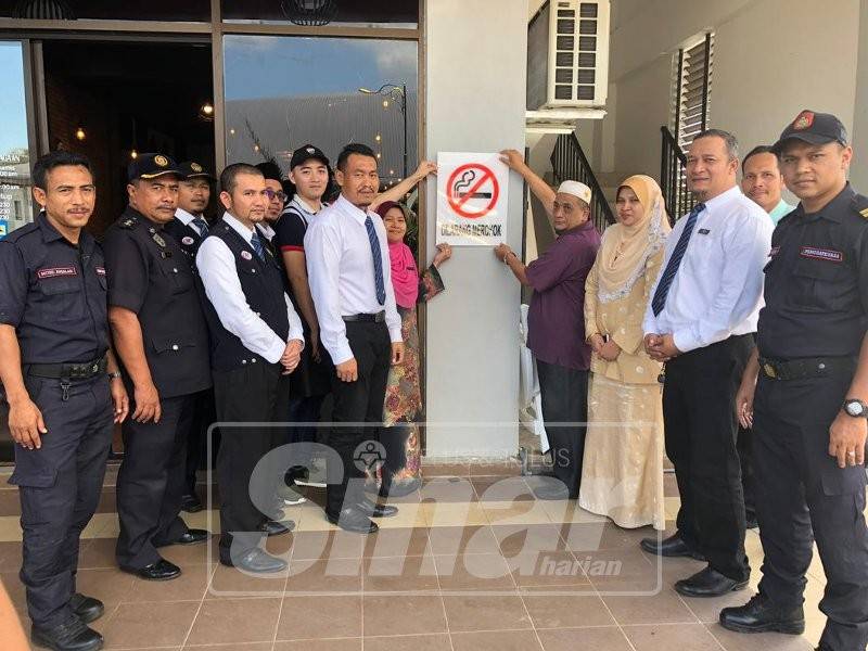 Siti Mariam (kiri) dan Lob di samping Razan (tiga, kanan) memasang tanda larangan merokok di sebuah restoran di Kampung Raja tengah hari tadi.