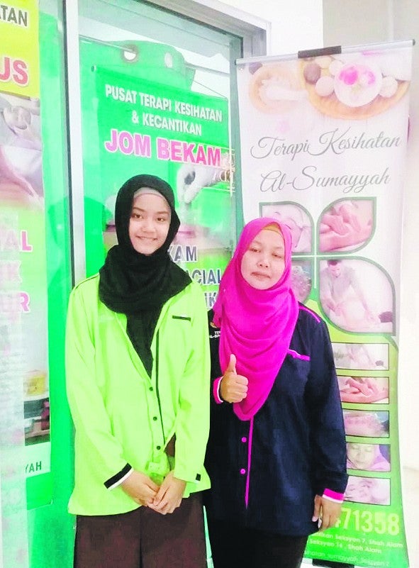 Latipah (kanan) bersama salah seorang kakitangan di hadapan premis terapinya.