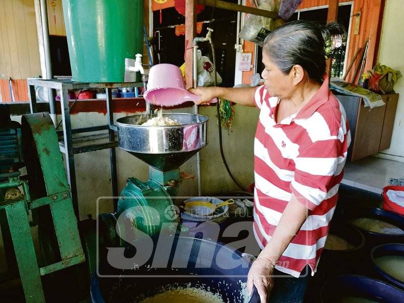 Che Minah mengisar beras pulut.