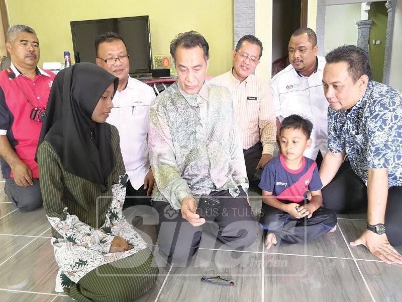 Nur Shazana (kiri) menunjukkan gambar ibunya di dalam telefon bimbit kepada Husam yang menziarahi mereka di Kampung Bukit Kechik.