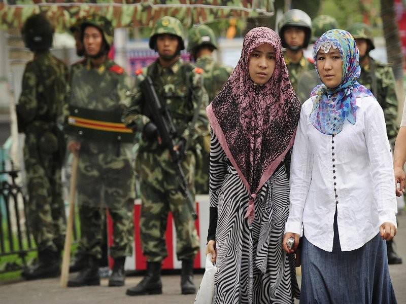 Dua wanita etnik Uighur tenang melalui sebatang jalan yang dipenuhi sekumpulan tentera China di wilayah Xinjiang.