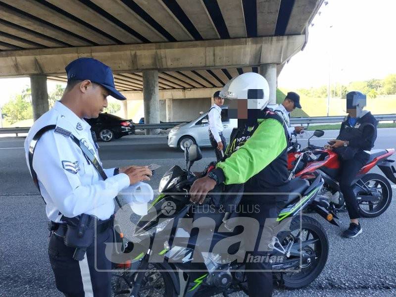 Anggota polis mengeluarkan saman kepada penunggang motosikal yang melakukan kesalahan trafik.