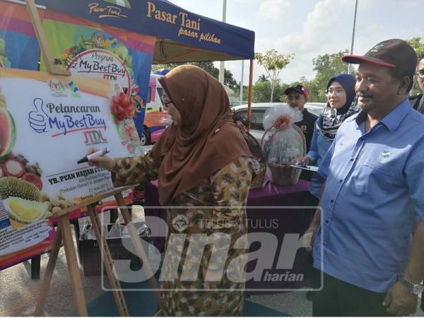 Fuziah menyempurnakan gimik pelancaran Program My Best Buy dan Jualan Terus Dari Ladang di Serambi Teruntum disaksikan Rosli.
