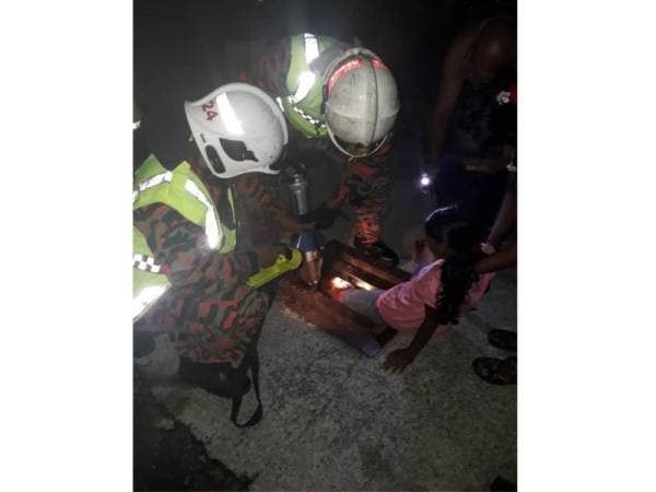 Anggota bomba berusaha meregangkan jaring besi penutup longkang bagi membantu melepaskan kaki kiri mangsa yang tersepit di tempat kejadian malam tadi.