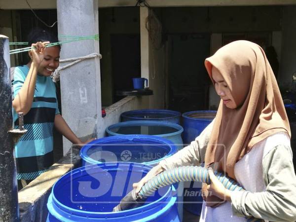 Siti Ain (kanan) dan Siti Aminah menunggu bekalan air yang dihantar oleh petugas.