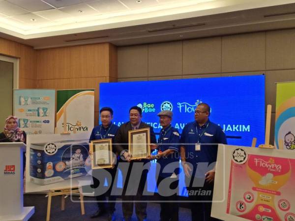 Dr. Sirajuddin (dua, kiri) menyerahkan sijil halal untuk produk lampin pakai buang dan tuala wanita keluaran Bio Integrasi Global Sdn Bhd sambil diperhatikan oleh Shahrizal (kanan) dan Kon Foon (kiri).