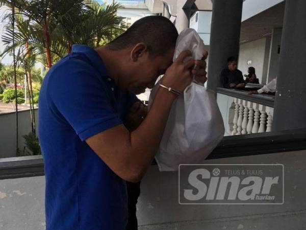 Mohd Nur Baderyshah cuba menutup muka ketika gambarnya dirakam petugas media di pekarangan Mahkamah Sesyen di Ayer Keroh, hari ini.