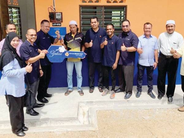 Mohd Zaki Yamani (empat dari kiri) menerima replika kunci yang diserahkan Syed Nasser Hussain (tiga dari kiri) sewaktu Majlis Penyerahan Kunci Rumah Asnaf Bank Rakyat di Kampung Pasir Dula.