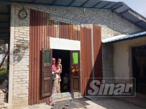 Rohani berdiri di hadapan pintu rumahnya yang mana dinding terpaksa ditampal dengan atap zink.