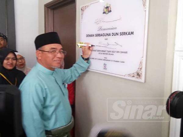 Adly menurunkan tandatangan plak perasmian di luar bangunan dewan serbaguna itu.