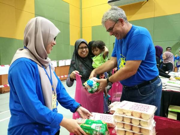 Michael (kanan) membantu sukarelawan mengagihkan barangan kepada penerima.