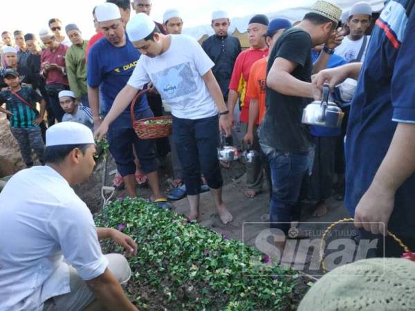 Salah seorang ahli keluarga Allahyarham menyiram air di pusara selepas selesai acara pengebumian.