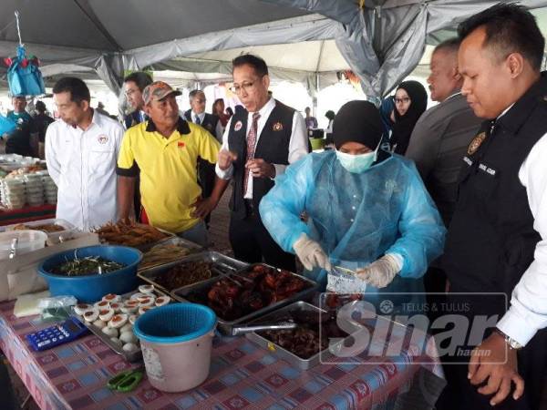 Dr Norhizan (tengah) memberikan penerangan kepada penjual makanan mengenai sampel makanan yang perlu diambil untuk tujuan pemeriksaan di Bazar Ramadan Pokok Sena hari ini.