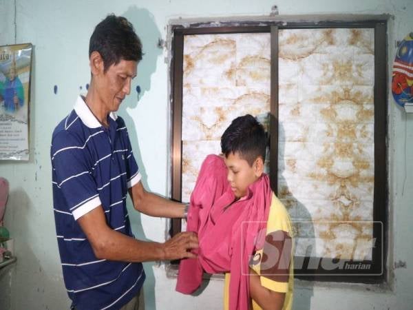 Hun Kheng memakaikan baju Melayu yang disumbangkan pihak sekolah kepada anaknya.