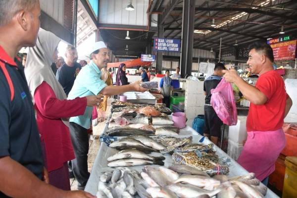 Ahmad Shah menyerahkan sumbangan kurma kepada salah seorang peniaga ikan di Pasar Chabang Tiga, Kuala Terengganu.
