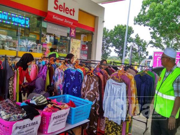 Zulkifly (kanan) melihat beberapa orang yang sedang melihat pakaian yang diletakkan di ruang depan stesen minyak Shell miliknya.