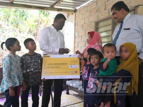 Arul Kumar menyerahkan replika cek kepada Nor Azila mewakili anak Allahyarham sambil diperhatikan Nallusamy (kanan).