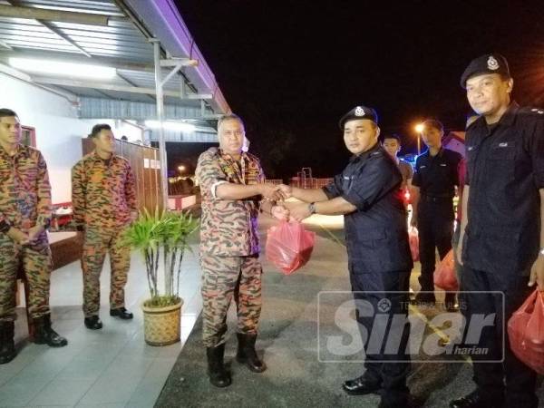 Hasron (kanan) menyerahkan pek makanan kepada penyelia bertugas di Balai Bomba dan Penyelamat Kampar, Mohd Shariman Yusoff.