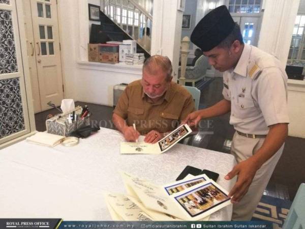 Sultan Ibrahim sedang menurunkan tanda tangan pada kad raya. - Foto ROYAL PRESS OFFICE
