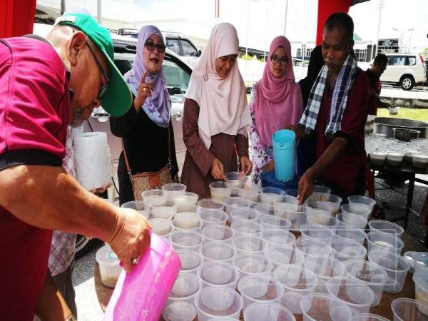 Nor Azrina (tengah) mengagihkan bubur lambuk yang siap dimasak kepada orang ramai.
