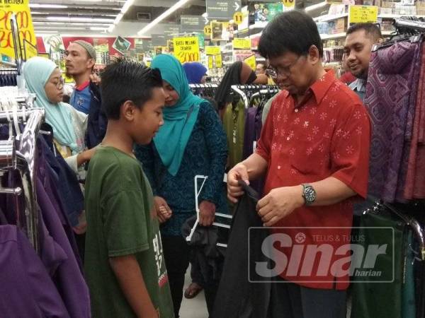 Asmuni (kanan) turut sama membantu memilih pakaian untuk anak-anak yatim terpilih menerima sumbangan berkenaan.