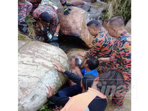 Anggota bomba berusaha mengeluarkan tangan remaja mangsa yang tersepit di celah batu terbabit.