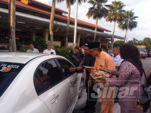 Ahmad Ishak (tengah) mengedarkan goodies beg kepada pengguna di hentian tersebut, kelmarin.