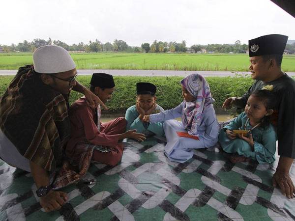 Amran Yahya, 50, (kanan) melayan keletah cucu jagaannya (dari kanan) Nur Airis Humaira Mohd Afiza, 4, Nur Airiena Harissha Mohd Afiza, 9, Muhammad Airiel Hakeem Mohd Afiza, 11, dan Muhammad Amin Hazeem Zulkifli, 12, bermain ketika menyambut Aidilfitri di Kampung Lonek hari ini. - Foto Bernama