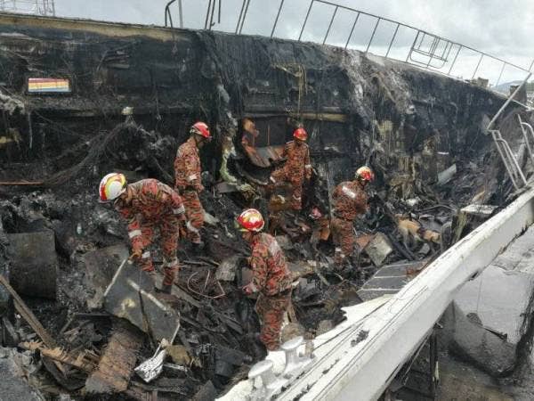 Anggota bomba mengeluarkan mayat mangsa yang ditemui rentung di bawah sisa kebakaran bot mewah di kawasan pembaikan di Bukit Malut. - FOTO JBPM KEDAH
