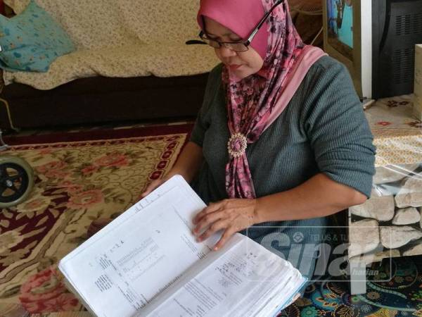 Noraini melihat buku rekod berkaitan kesihatan anaknya.