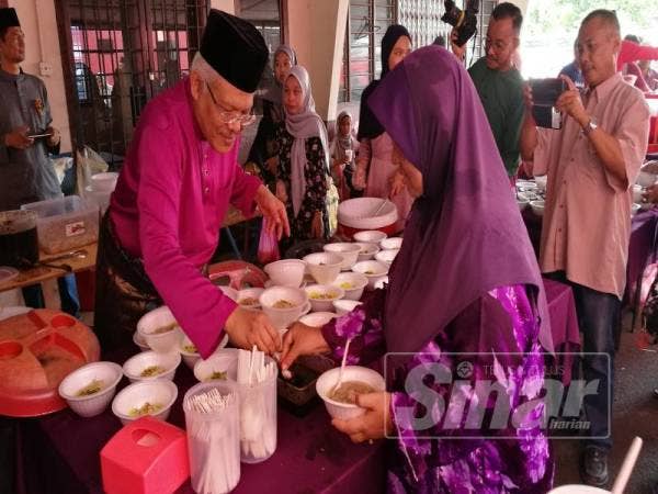 Hamzah (kiri) turut membantu tetamu yang hadir mengambil pelbagai juadah raya disediakan pihaknya hari ini.