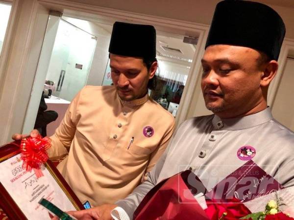 Ahmad Shah Rizal (kanan) mengamati anugerah yang diterima bersama adik iparnya, Mohd Faizul Rohban bagi pihak Allahyarham Faziani Rohban selepas Sambutan Hari Sayyidatina Khadijah hari ini.