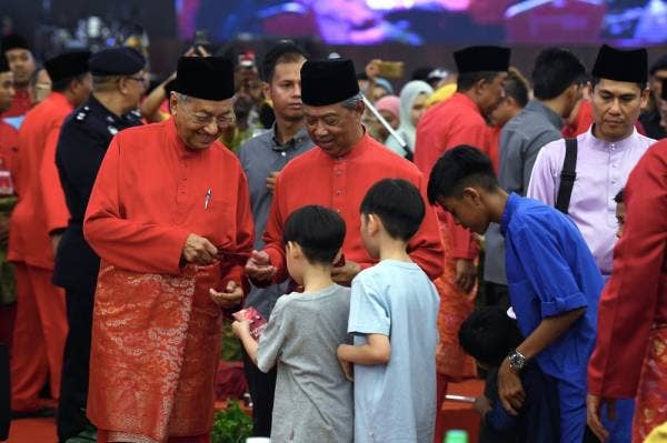Dr Mahathir dan Muhyiddin menyampaikan duit raya kepada kanak-kanak pada Majlis Rumah Terbuka Hari Raya Aidilfitri PPBM peringkat kebangsaan di Dewan Konvensyen MBI Desaku Kulim Hi-Tech Park hari ini. -Foto Bernama
