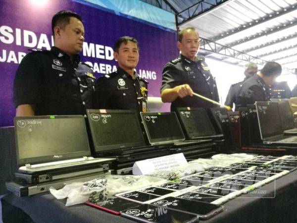 Ahmad Dzaffir (kanan) menunjukkan rampasan komputer riba dan telefon bimbit yang dirampas dalam serbuan di sebuah unit kondominium dijadikan sebagai pusat judi dalam talian antarabangsa di Sungai Long, Kajang, pada 28 Jun lalu.