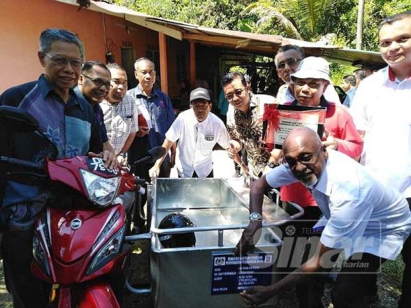 Sivarasi melekatkan pelekat penerima bantuan program PPP pada coley Ku Muda (tiga dari kanan) sambil disaksikan Mustapa (kiri) sebagai simbolik penyerahan bantuan berkenaan, di sini hari ini.