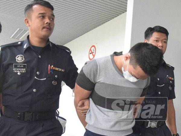 Tertuduh (tengah) diiringi anggota polis selepas mengaku tidak bersalah di Mahkamah Sesyen Ayer Keroh di sini hari ini atas pertuduhan melakukan rompakan dan mencederakan seorang guru di parkir sebuah pusat beli-belah pada minggu lalu.