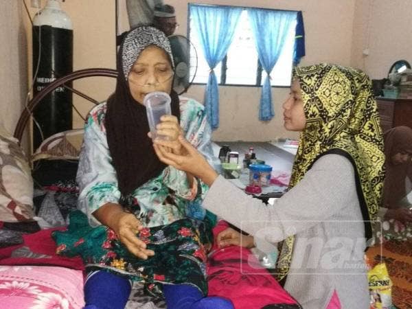Zulaila memberikan air kepada ibunya yang menghidap kanser payudara di rumah mereka di Kampung Rambah.