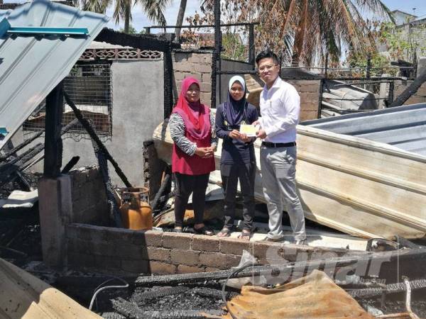 Chuan How (kanan) menyerahkan sumbangan kepada Nur Fazira (tengah) disaksikan ibunya, Hamisah Din di kawasan kediaman atlet itu yang terbakar di Kuala Bagan Tiang, Parit Buntar hari ini.